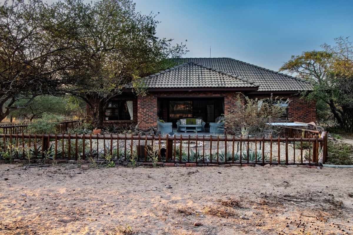 Rear view of a brick-built house featuring a covered patio area, tiled roof, and a rustic timber-fenced garden setting.
