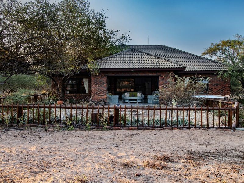 Rear view of a brick-built house featuring a covered patio area, tiled roof, and a rustic timber-fenced garden setting.
