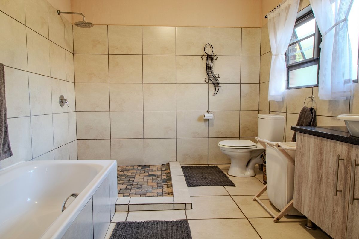 A functional bathroom featuring a built-in bathtub, a separate walk-in shower with stone-look tiling, a toilet, and a vanity cabinet with a vessel sink.