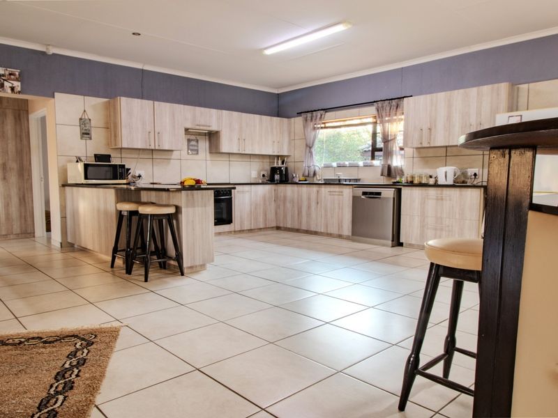 Spacious open-plan kitchen featuring light wood-finish cabinetry, tiled flooring, a breakfast counter, and integrated appliances, offering a functional and well-maintained cooking and living space.