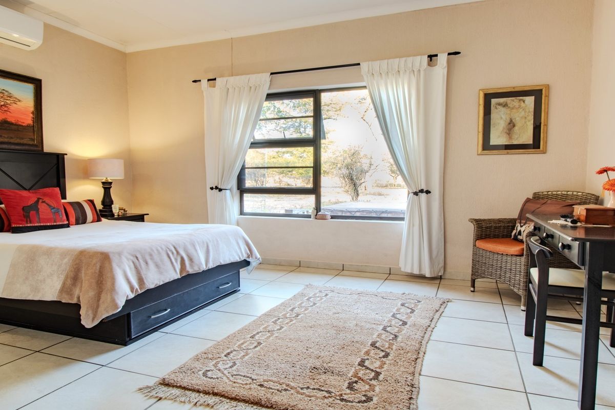 A well-lit bedroom featuring tiled flooring, an aluminium-framed window, and a wall-mounted split-system air conditioner.