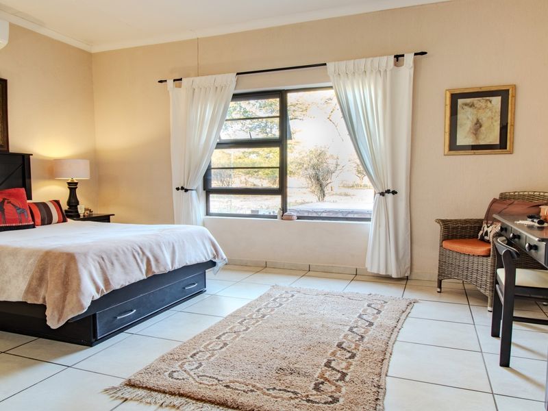 A well-lit bedroom featuring tiled flooring, an aluminium-framed window, and a wall-mounted split-system air conditioner.