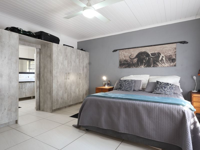 Spacious bedroom featuring built-in cupboards, tiled flooring, and a ceiling fan, with an adjoining en-suite bathroom.