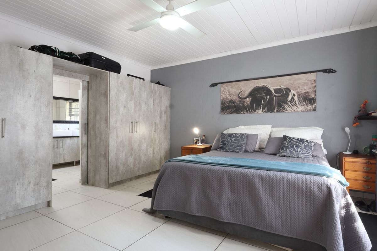 Spacious bedroom featuring built-in cupboards, tiled flooring, and a ceiling fan, with an adjoining en-suite bathroom.