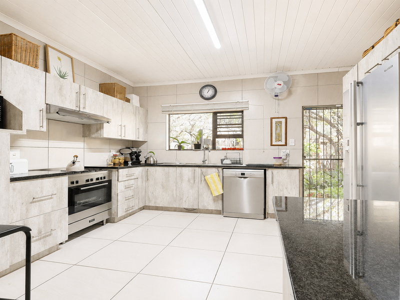 A functional kitchen featuring light wood-look cabinetry, granite countertops, stainless steel appliances, tiled flooring, and direct access to the rear garden.