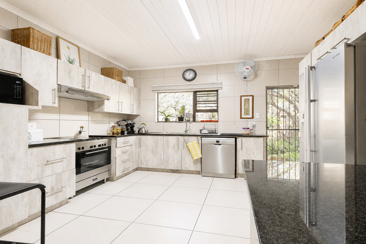 A functional kitchen featuring light wood-look cabinetry, granite countertops, stainless steel appliances, tiled flooring, and direct access to the rear garden.