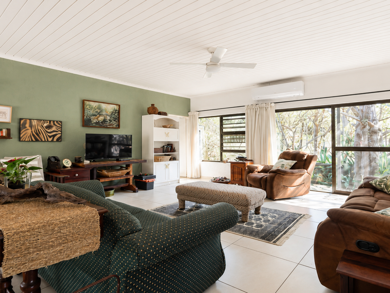Spacious living room featuring tiled flooring, a ceiling fan, split-system air conditioning, and large sliding glass doors providing natural light and garden views.