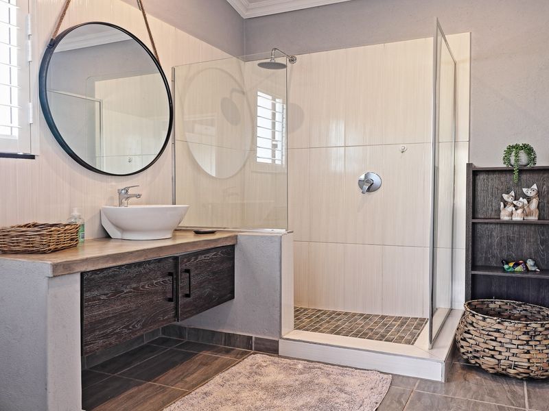 Modern bathroom featuring a walk-in shower with glass screen, vessel sink vanity, and neutral wall tiling.