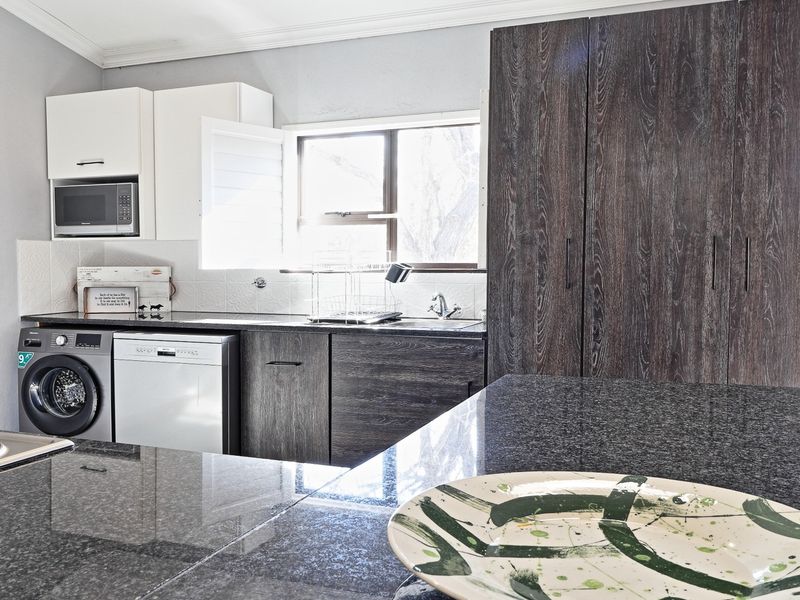 Modern kitchen featuring dark wood cabinetry, granite countertops, tiled backsplash, and integrated appliances, offering a functional and stylish workspace.