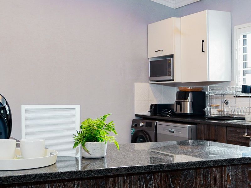 A functional kitchen featuring dark wood cabinetry, granite countertops, a tiled backsplash, and integrated appliances including a dishwasher and microwave.