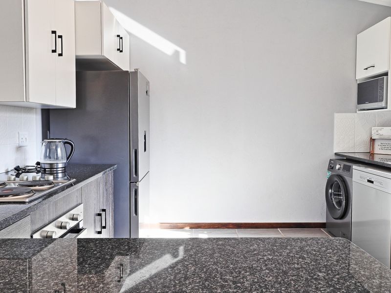 Modern kitchen featuring granite countertops, built-in oven, electric hob, and ample cabinetry with integrated space for laundry appliances.