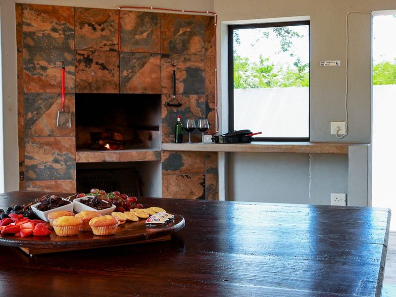 Covered patio area featuring a built-in braai with stone tile cladding and a concrete prep counter, overlooking the garden.
