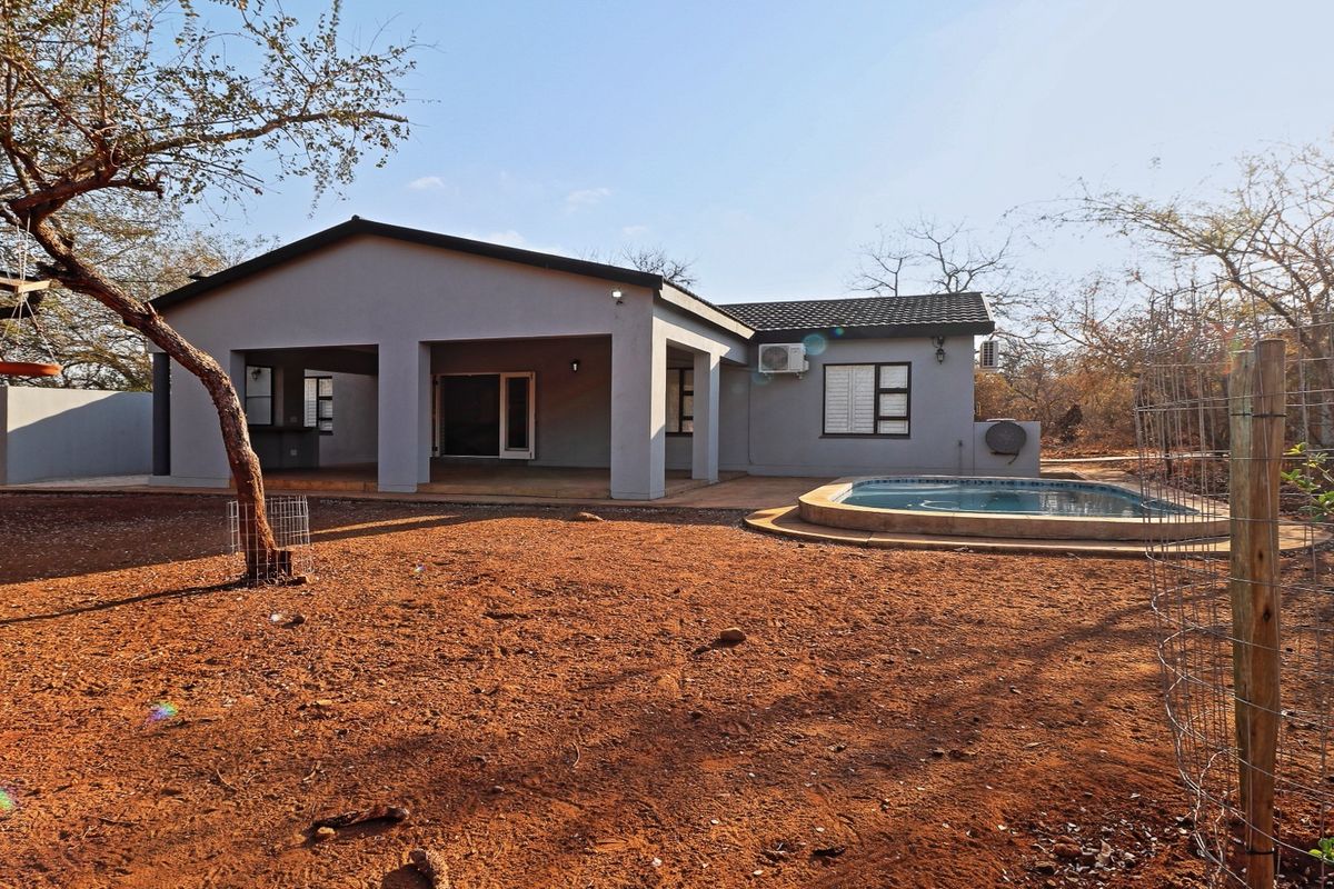 Rear view of the house featuring a covered patio area and a swimming pool set within a large, natural garden space.