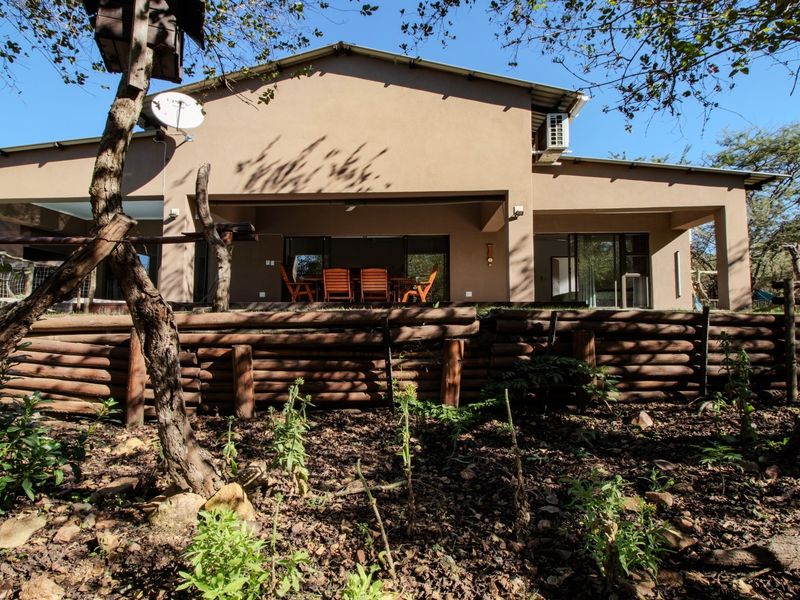 Rear view of the house featuring a covered patio, sliding glass doors, and a timber retaining wall set within a natural garden landscape.