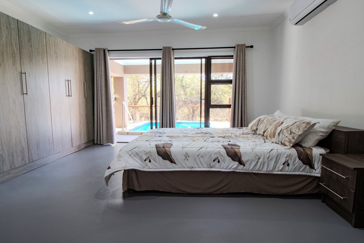 Spacious bedroom featuring extensive built-in cupboards, a ceiling fan, air conditioning, and sliding glass doors providing direct access to the pool area.