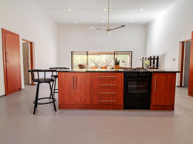 Modern kitchen featuring a central island with a built-in oven, gas hob, and polished concrete flooring, opening to an outdoor area.