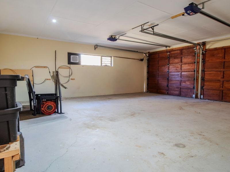 Spacious double garage featuring automated wooden doors, concrete flooring, and a small side window for natural light.