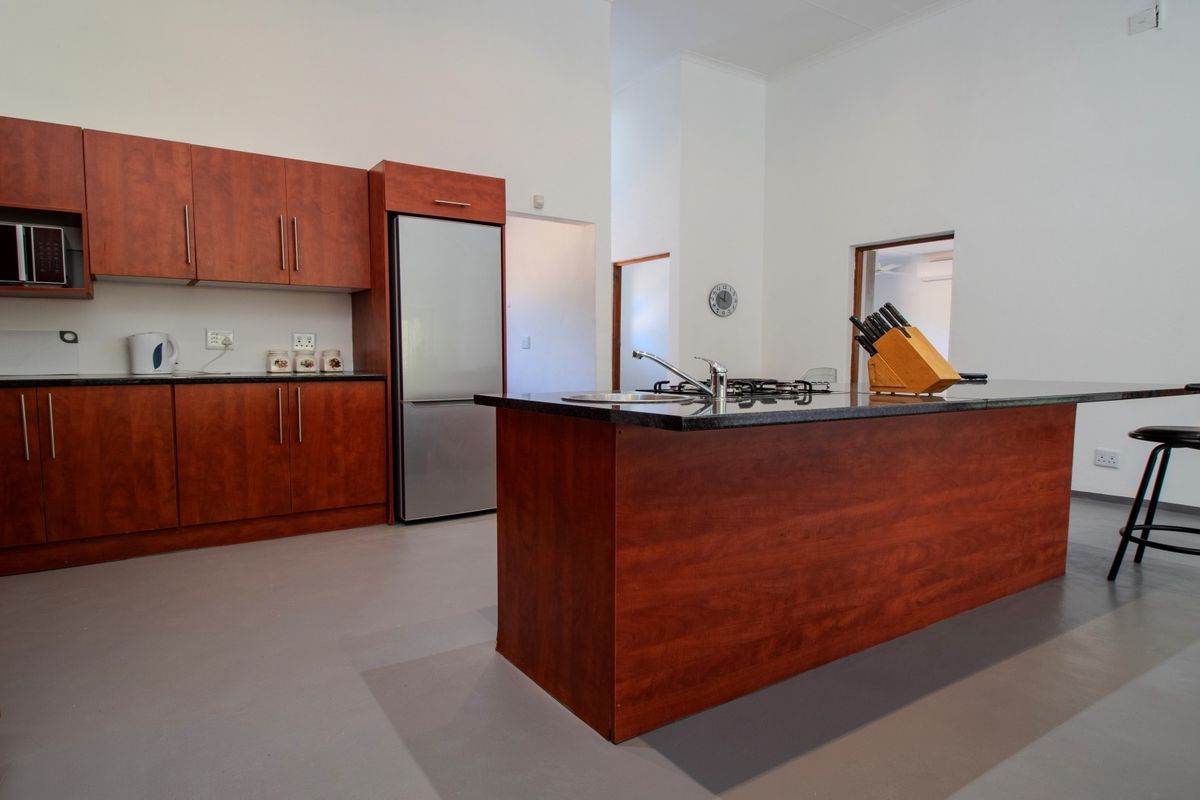A spacious kitchen featuring cherry wood cabinetry, granite countertops, a central island with a gas hob, and modern finishes.