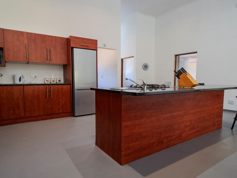 A spacious kitchen featuring cherry wood cabinetry, granite countertops, a central island with a gas hob, and modern finishes.