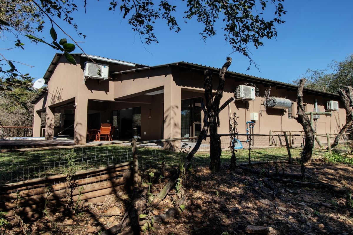 Rear view of the house featuring a covered patio, multiple air conditioning units, and external plumbing fixtures set against a natural bushveld backdrop.
