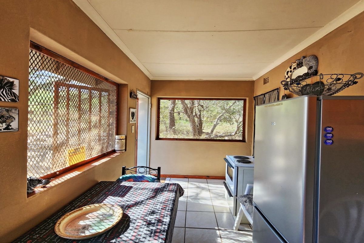 A functional kitchen area featuring tiled flooring, security screen windows, and a freestanding stove, offering a practical layout with potential for modernization.