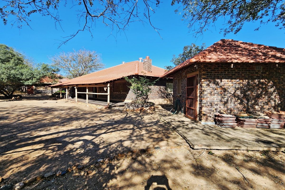Rear view of a brick house featuring a tiled roof, covered patio area, and a chimney, set within a natural, rustic garden environment.
