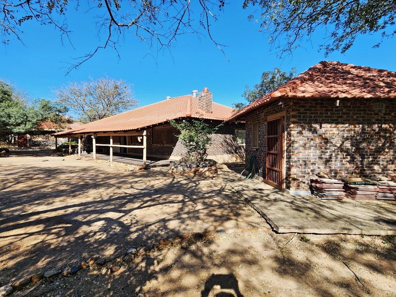 Rear view of a brick house featuring a tiled roof, covered patio area, and a chimney, set within a natural, rustic garden environment.