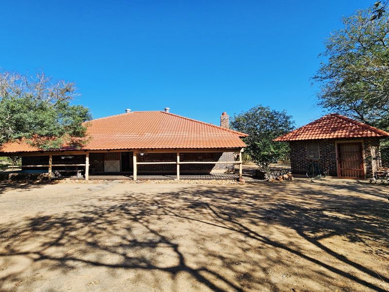 Rear view of a rustic brick house featuring a terracotta tile roof, a covered veranda with timber railings, and a separate matching outbuilding.