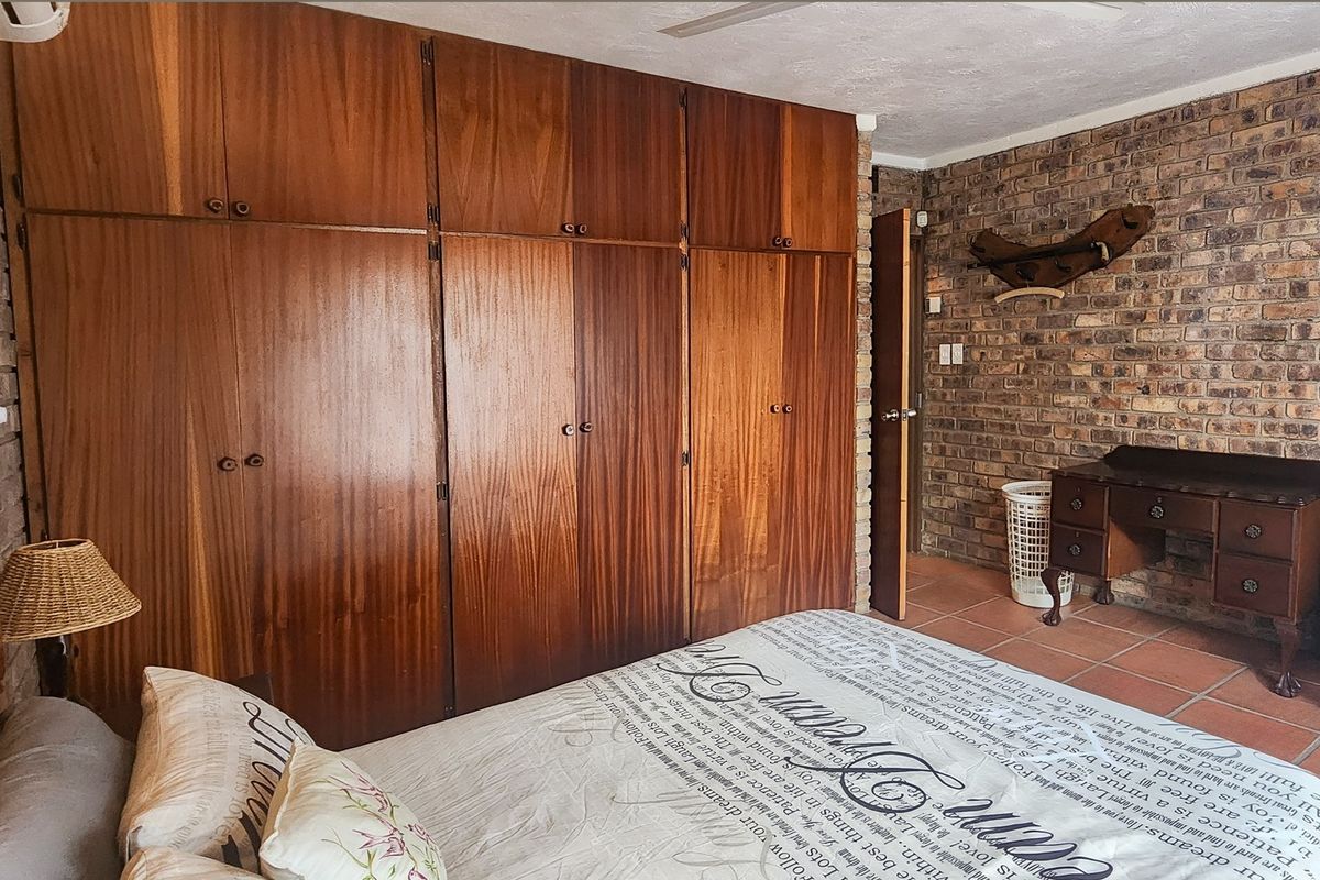 A bedroom featuring extensive built-in wooden cabinetry, exposed brick feature walls, and tiled flooring, offering a rustic aesthetic with ample storage space.