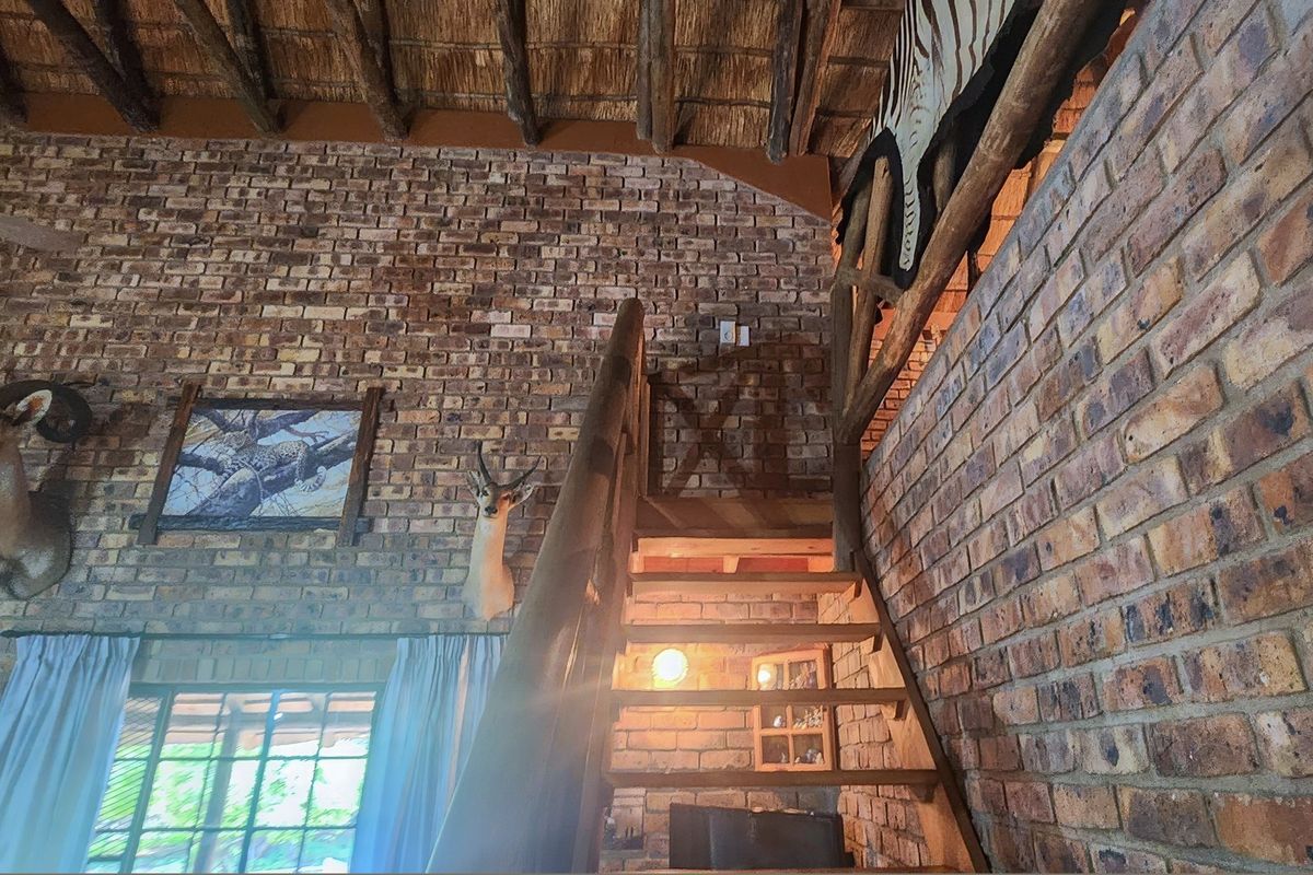 Rustic living area featuring exposed brick walls, a high thatched ceiling with timber rafters, and a wooden staircase leading to an upper level.