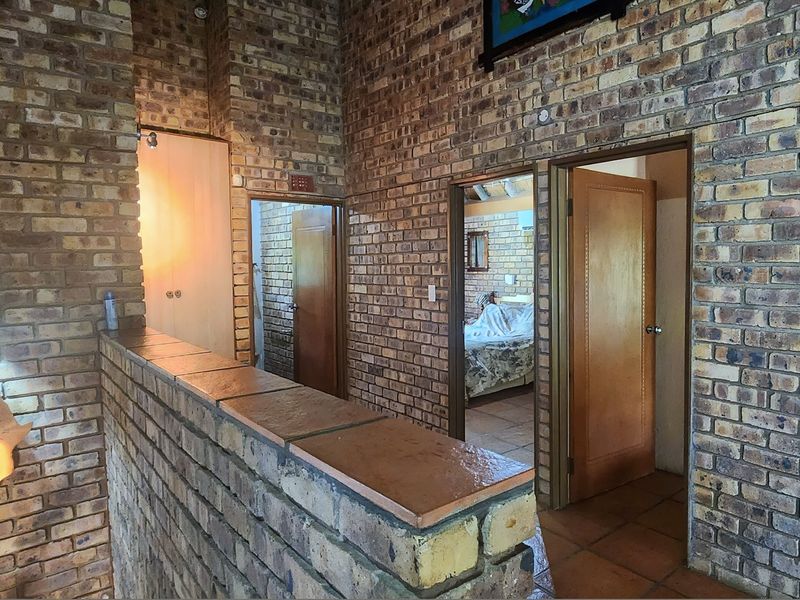 A rustic hallway featuring exposed brick walls, tiled flooring, and multiple wooden doors leading to adjacent rooms.