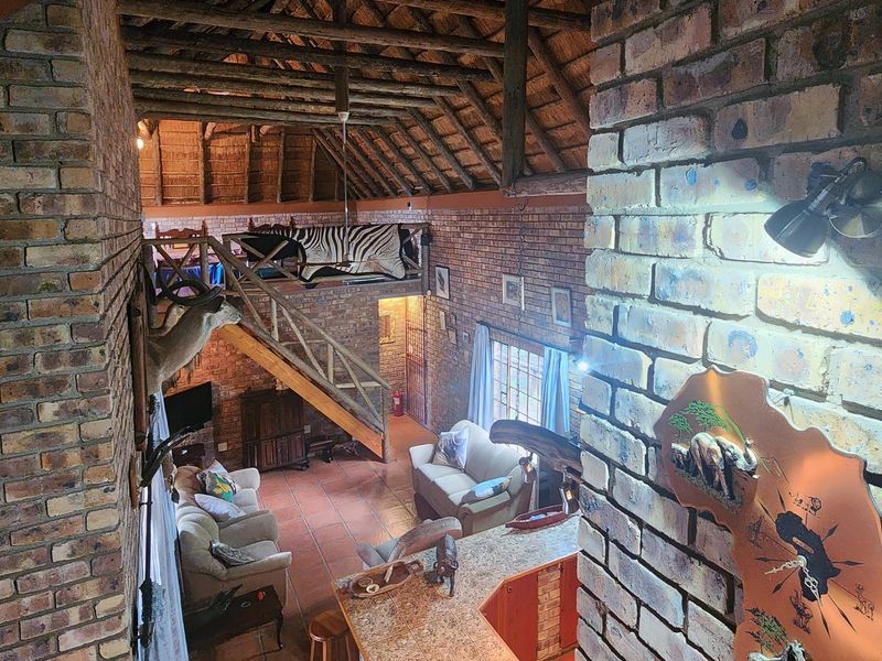 Spacious open-plan living area featuring high exposed thatch ceilings, facebrick walls, tiled floors, and a mezzanine level with a timber staircase.