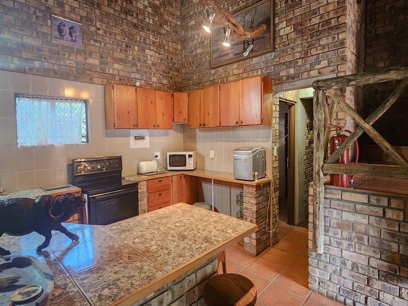 Rustic kitchen featuring exposed brick walls, wooden cabinetry, tiled countertops, and a functional layout with integrated stove and tiled flooring.