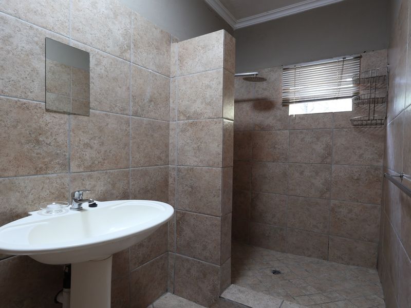 A functional bathroom featuring a pedestal basin, walk-in shower with tiled finishes, and a wall-mounted grab rail.