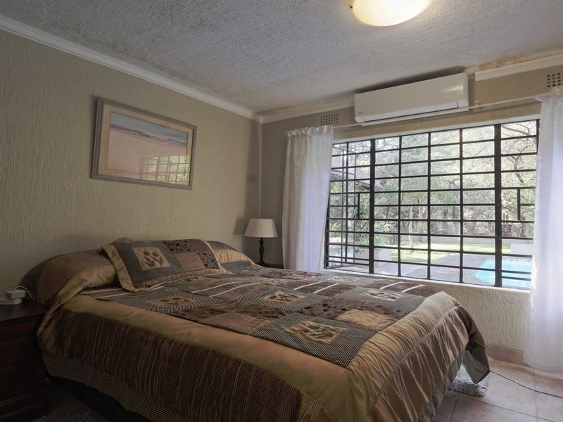 A bedroom featuring tiled floors, security bars on the window, and an air conditioning unit, showing signs of wear on the wall and ceiling.
