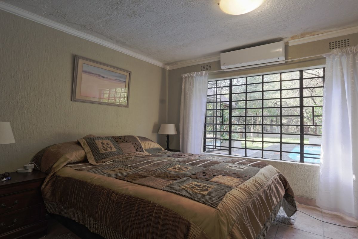 A bedroom featuring tiled floors, security bars on the window, and an air conditioning unit, showing signs of wear on the wall and ceiling.
