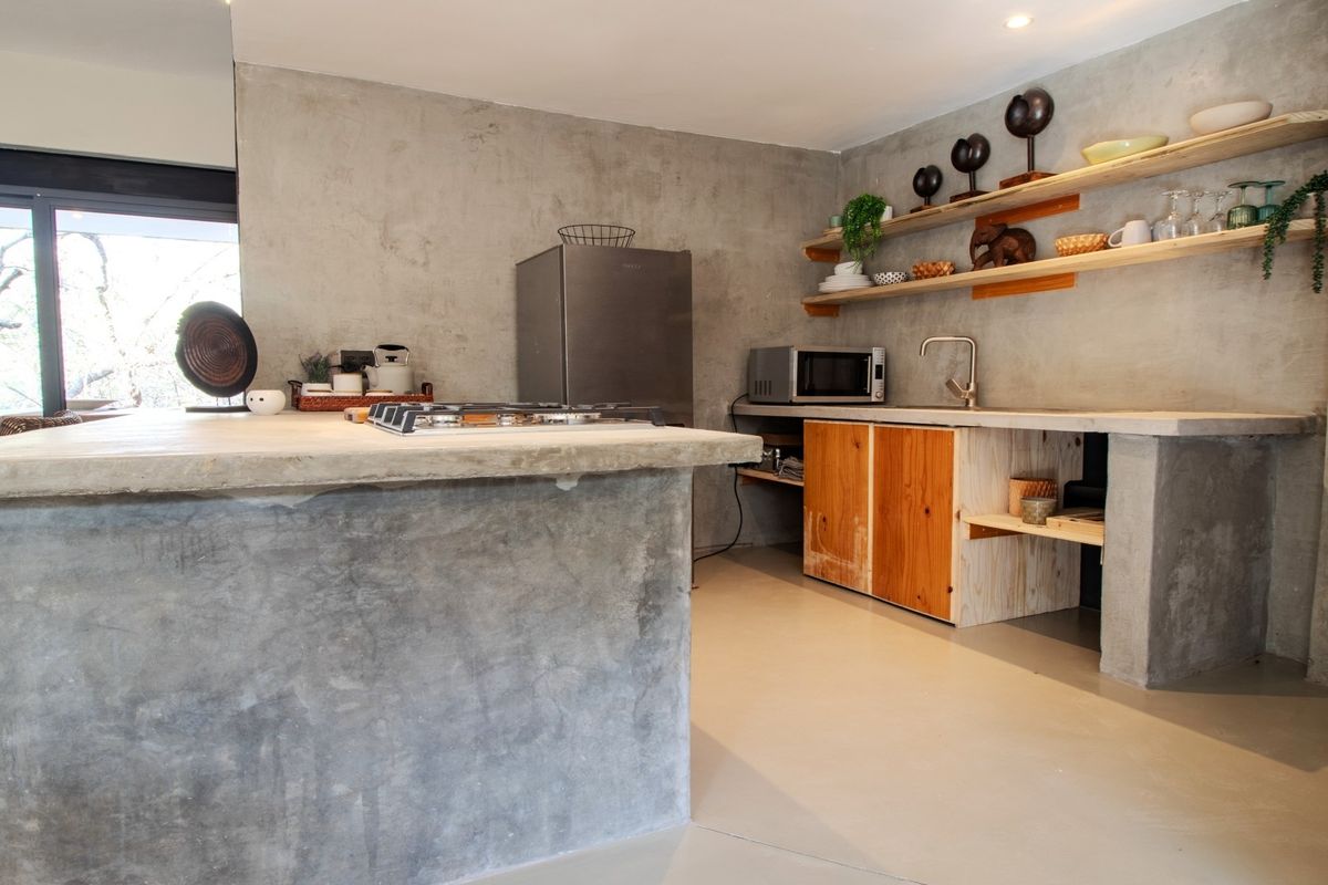 Modern industrial-style kitchen featuring concrete island and countertops, open timber shelving, and large sliding glass doors providing natural light.
