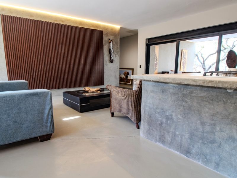 Modern open-plan living area featuring a concrete kitchen island, polished concrete floors, and a striking slatted timber feature wall with integrated lighting.