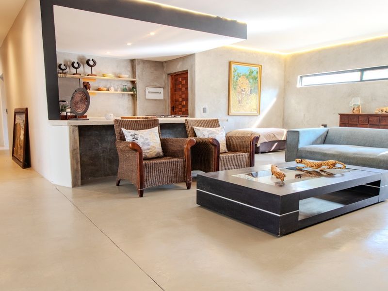 Spacious open-plan living area featuring polished concrete floors, modern recessed and cove lighting, and a contemporary kitchen breakfast bar.
