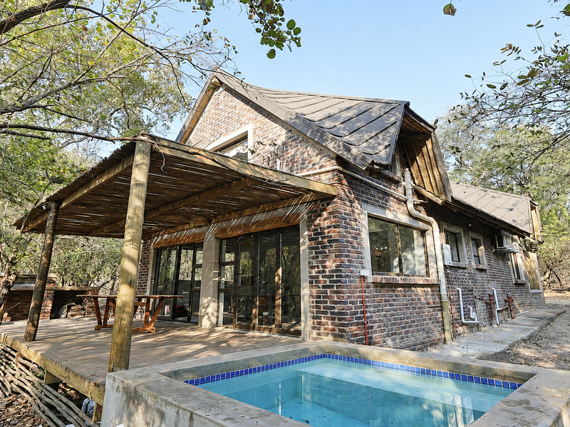 Rear view of a rustic brick house featuring a timber deck, covered patio, and a private plunge pool set within a natural wooded environment.