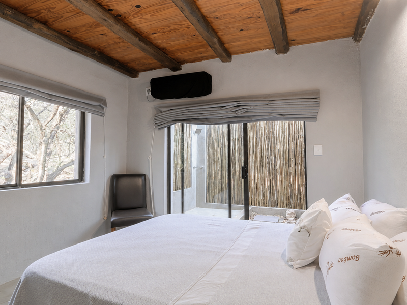 A bedroom featuring an exposed timber beam ceiling, large windows for natural light, and a sliding glass door leading to an outdoor area.
