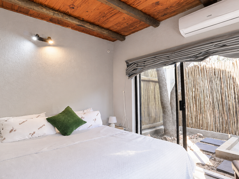 A cozy bedroom featuring an exposed timber ceiling, split-system air conditioning, and a sliding glass door providing direct access to a private outdoor area.
