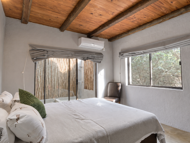 A well-maintained bedroom featuring exposed timber ceiling beams, polished concrete floors, a split-system air conditioner, and direct access to a private outdoor area.