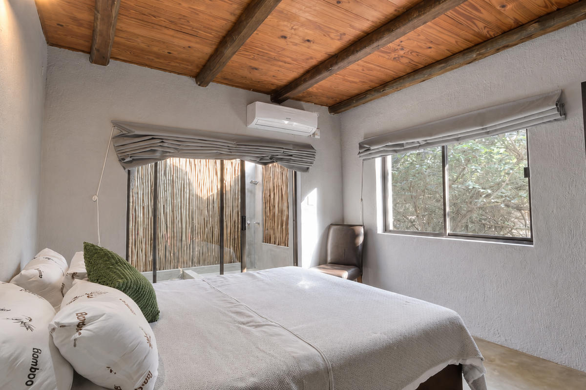A well-maintained bedroom featuring exposed timber ceiling beams, polished concrete floors, a split-system air conditioner, and direct access to a private outdoor area.