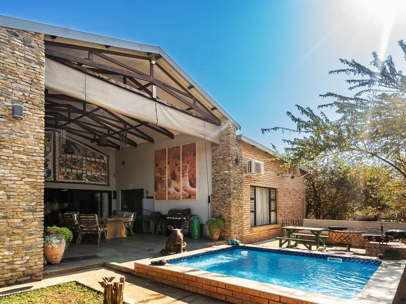 Spacious outdoor entertainment area featuring a covered patio with exposed timber trusses, stone-clad pillars, and a private swimming pool set in a landscaped garden.