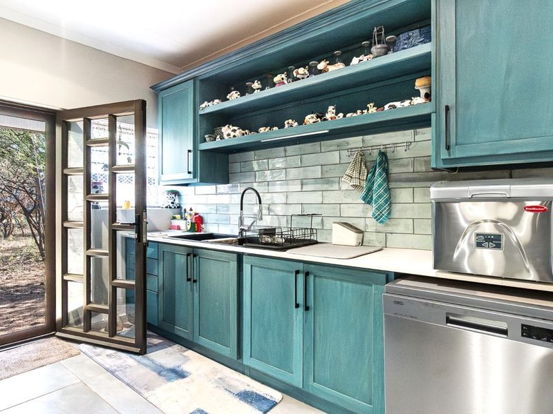 A functional kitchen featuring teal cabinetry, subway tile backsplash, and direct access to the outdoors through a glass-paneled door.