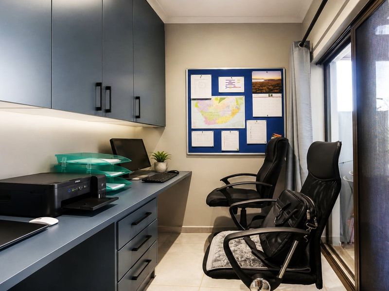A well-appointed home office featuring custom built-in cabinetry, integrated desk space, under-cabinet lighting, and direct access to an outdoor area via sliding glass doors.