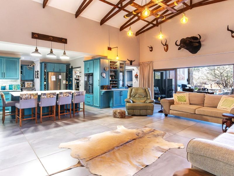 Spacious open-plan living area featuring a modern kitchen with blue cabinetry, a large island, and high vaulted ceilings with exposed timber rafters.