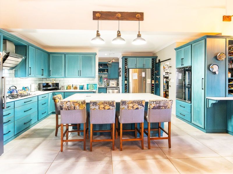 Spacious kitchen featuring vibrant blue cabinetry, a large central island with seating, integrated appliances, and modern pendant lighting.