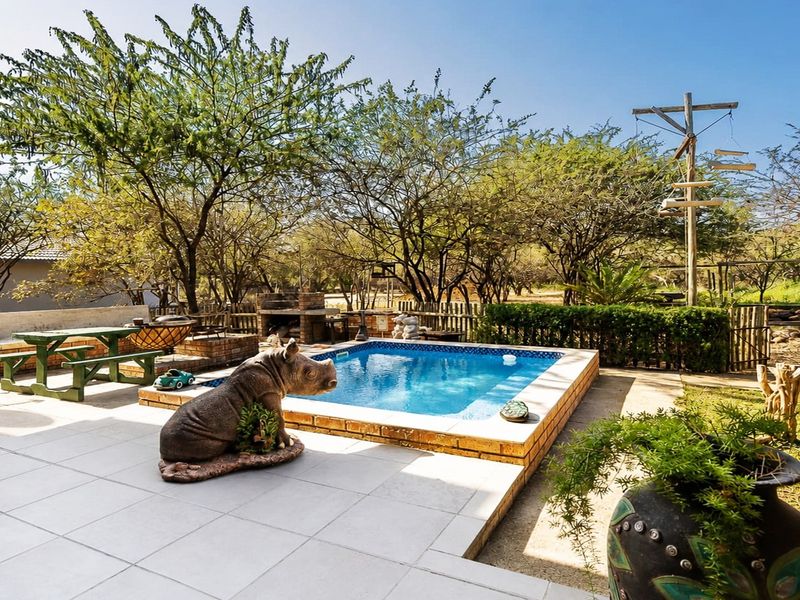 Outdoor entertainment area featuring a swimming pool, tiled patio, and a built-in brick barbecue, set within a landscaped garden environment.